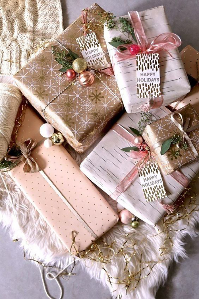 Vidám csomagolás arany és rózsaszín színekben különböző mintákkal, masnikkal, gömbdíszekkel és zöld növénykékkel.